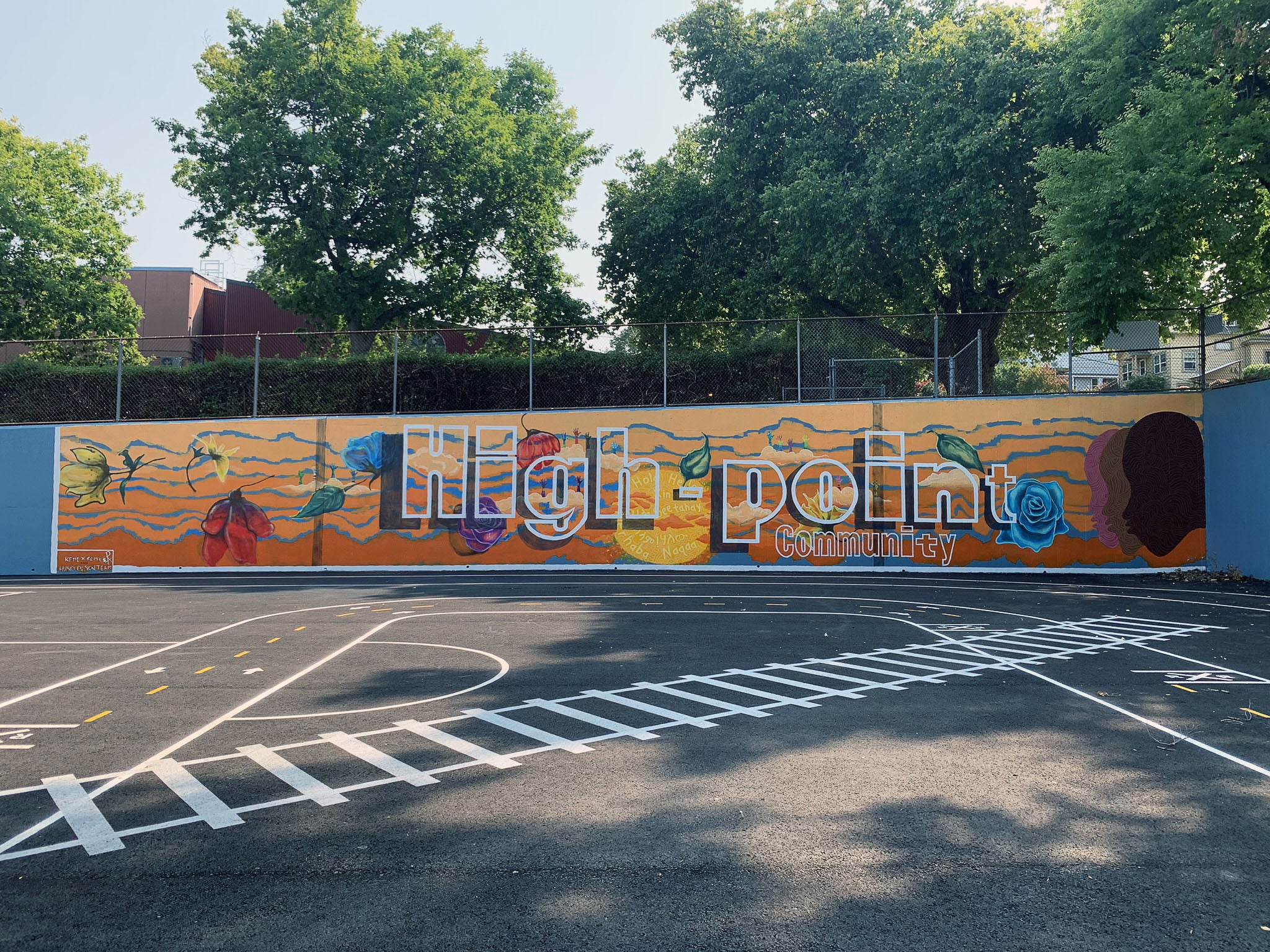 the wall of a paved play area has a mural painted on it that says High Point Community