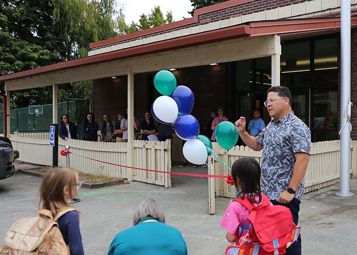 a man stands next to some helium balloons and a red ribbon stretched between silver stands