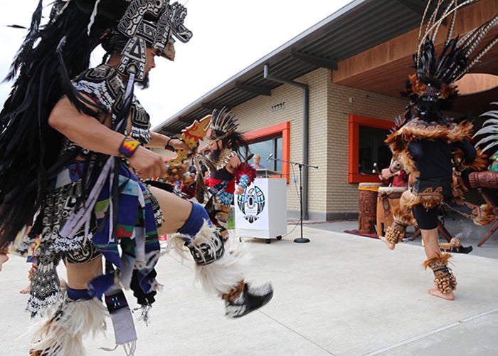 people in native dress dance in front of a 1 story building