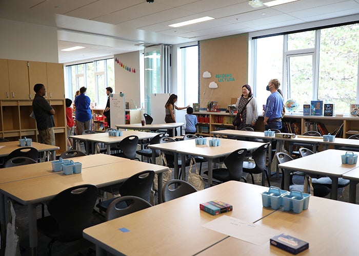 a classroom with groups of tables and a wall that is open to another classroom