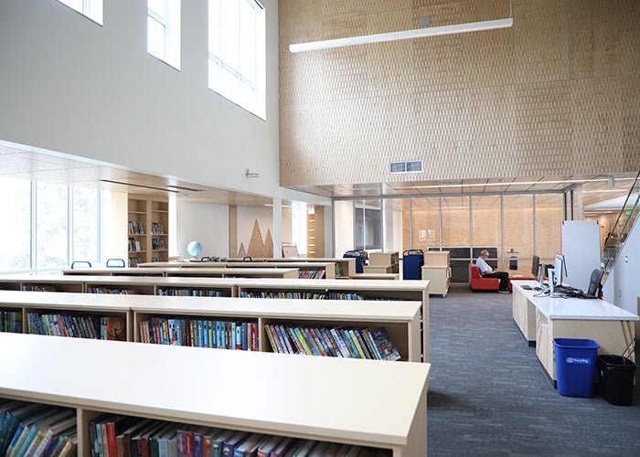 a large room has low bookshelves and a large wall of windows