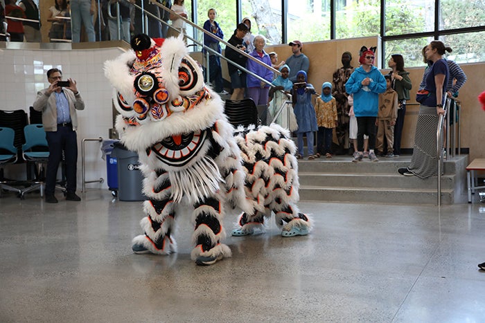 two people dressed in a white lion dancer costume at the bottom of a stairway with people watching from the stairs