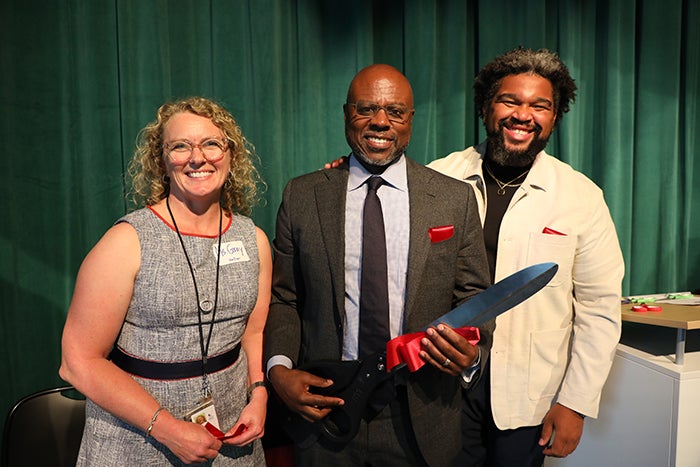 three people are shown from just below the waist. the one in the center holds giant scissors