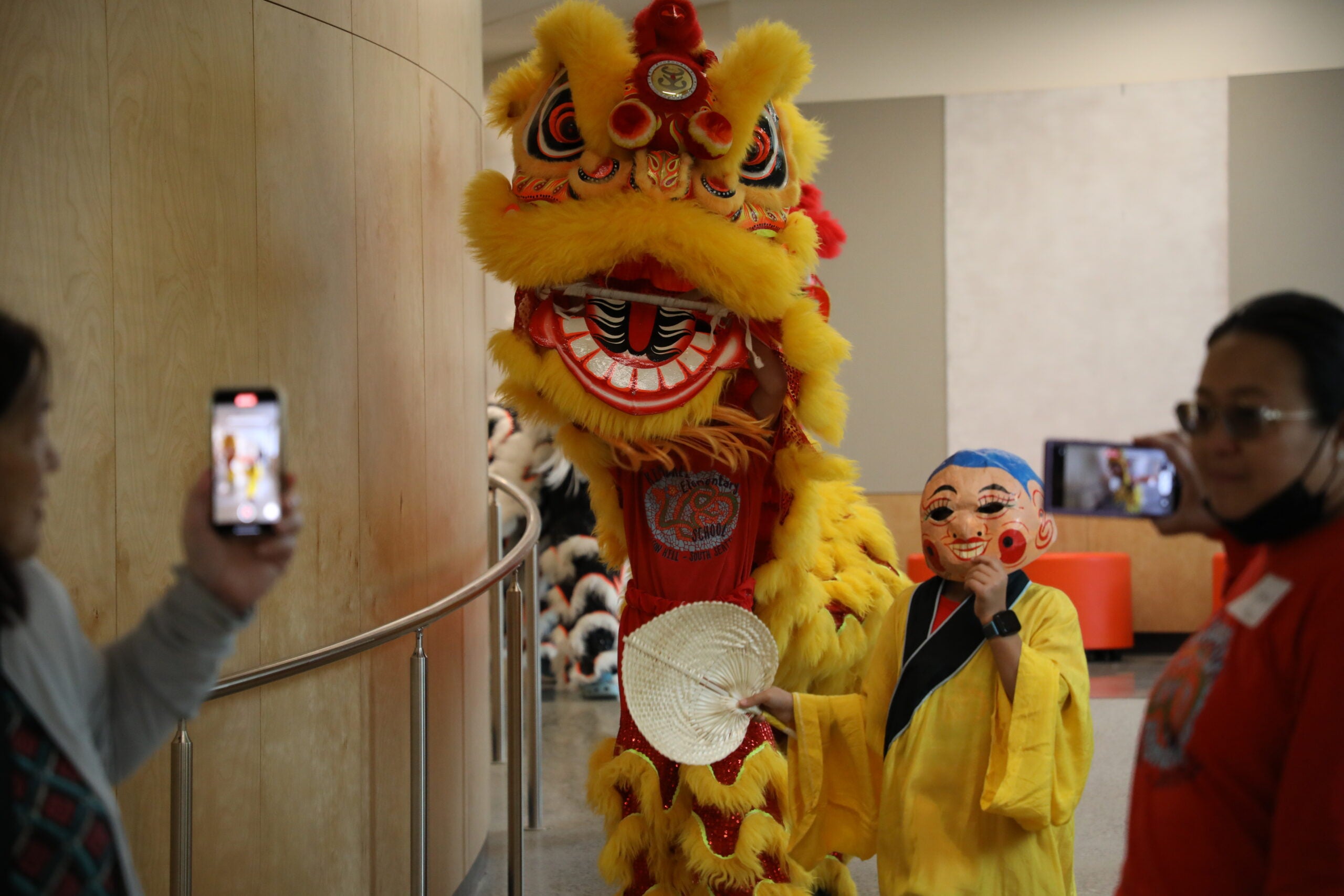 a yellow lion costume covers two people and a child holds a mask up next to it