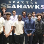 A large group of young men pose for a photo in front of a Seattle Seahawks sign