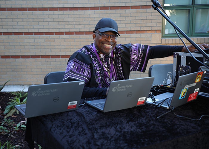 a man sits at a table with three laptops open and a microphone