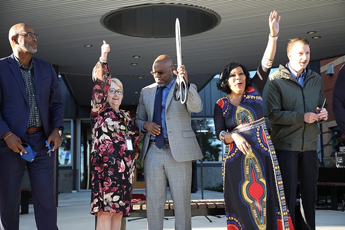 five people hold pieces of red ribbon and scissors with their hands up to cheer