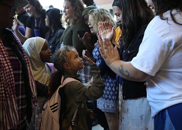 a child in a crowd of several children high fives an adult in a white shirt