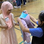 An adult helps a young child try on a new coat