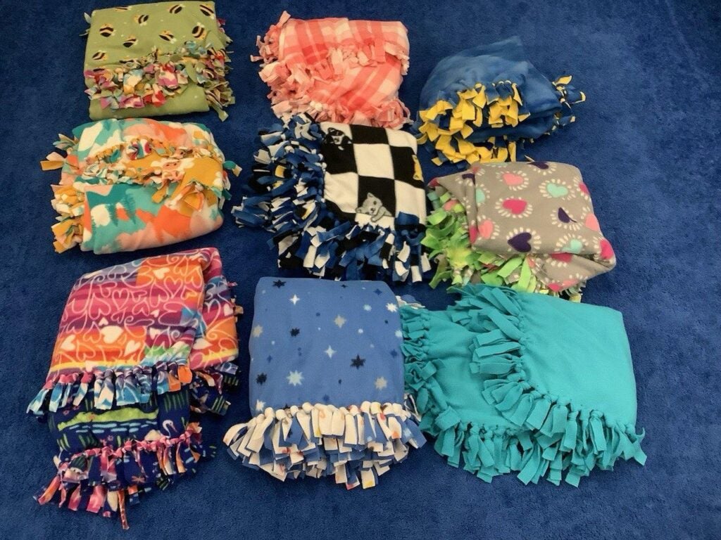 Nine folded tie blankets of various colors, arranged in squares