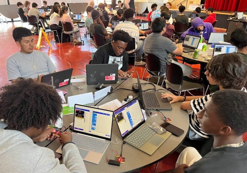 Five students sitting around round table working with Micro:Bits