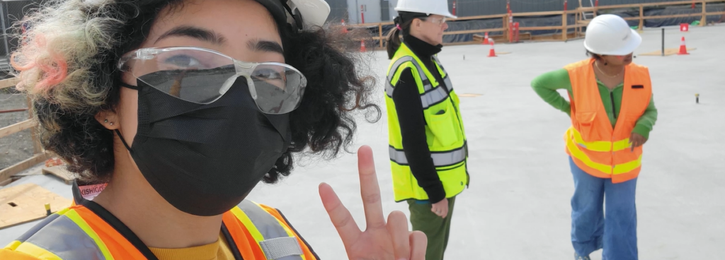 Student wearing mask holding up peace sign on construction job site
