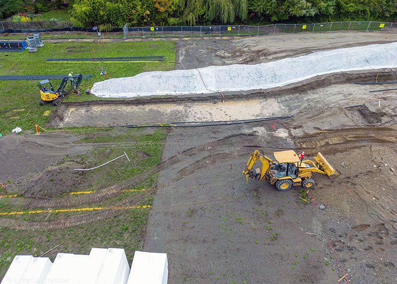 a construction site has a sloped dirt area that is next to a grass area. a back hoe and a bulldozer are in the photo