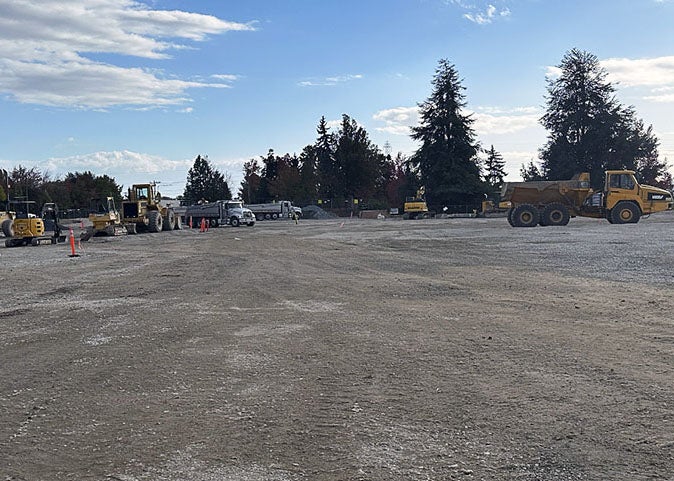 a large expanse of soil with construction vehicles. there are evergreen trees in the background.