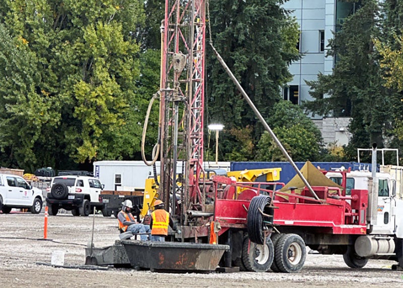 a tall metal structure is attached to the back of a truck with part of it in the ground. two workers are next to it.