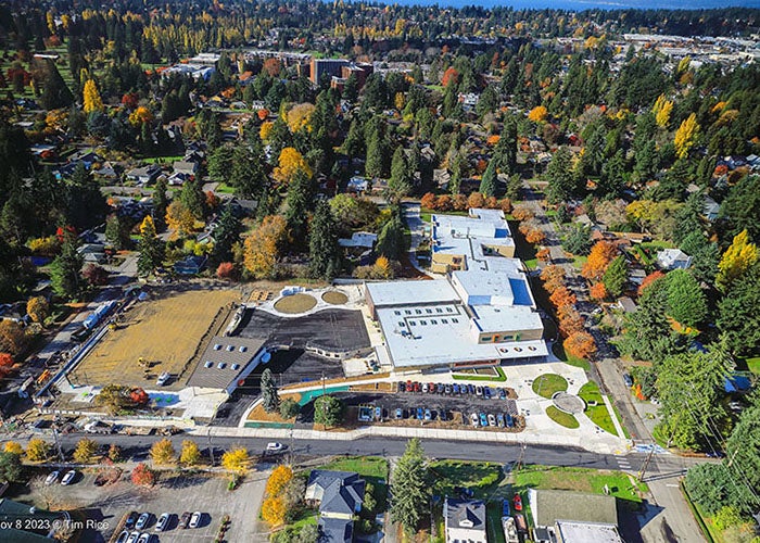 aerial view of a large building with a dirt field to the left and parking lots in front