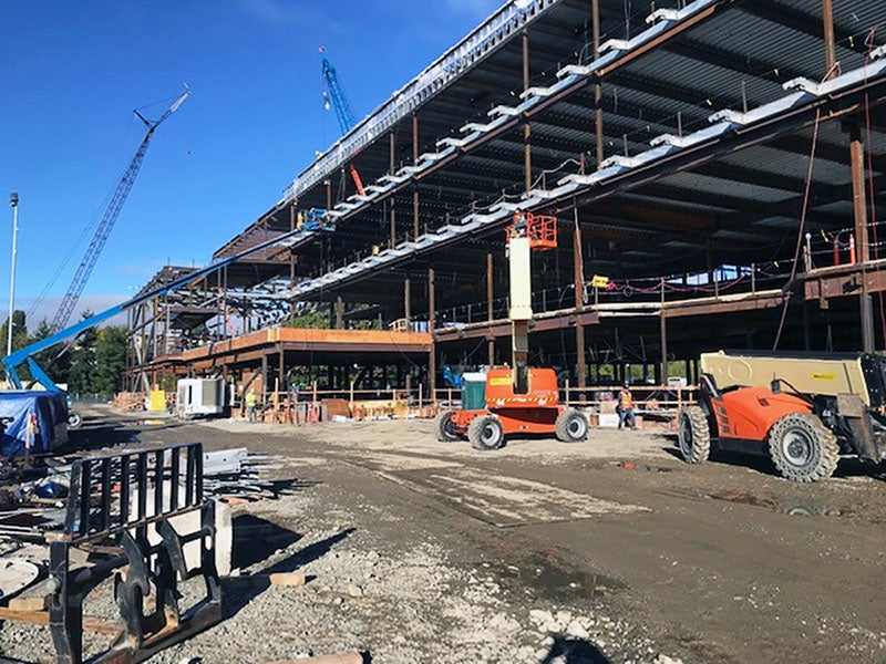 a four story steel frame for a large building with construction cranes, lifts, and other machines