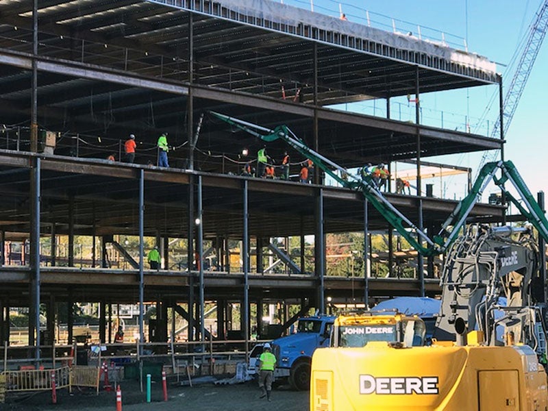 a concrete truck is pumping concrete to the third floor of a steel framed four-story building under construction