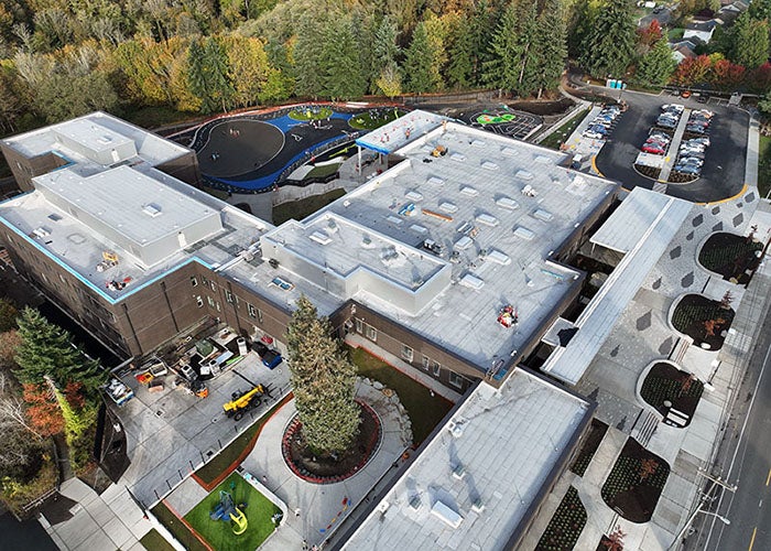 aeriel of a large building with a white roof with trees behind it