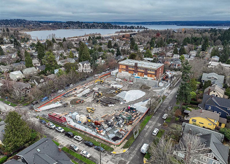 aerial view of a construction site with a brick building at one end and a view of a lake in the distance