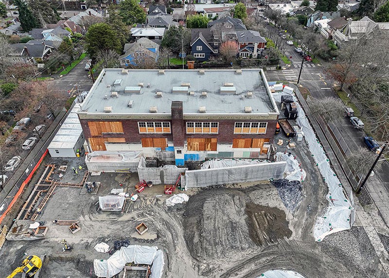 at brick building with boarded up windows sits in a construction site with a concrete wall in front