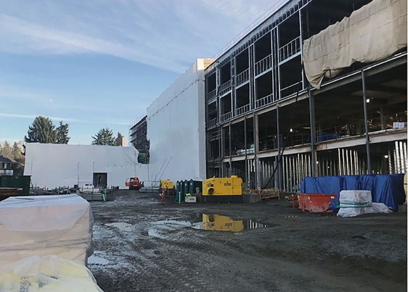 a four story frame of building has part of it wrapped in white material at a muddy construction site