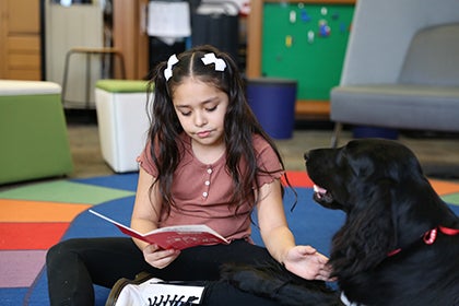 Wedgwood student in pink reads to Penny the dog.