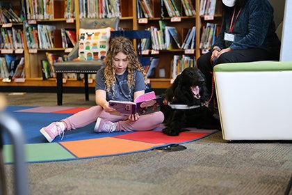 Wedgwood student in pink leggings reads to Penny the dog.
