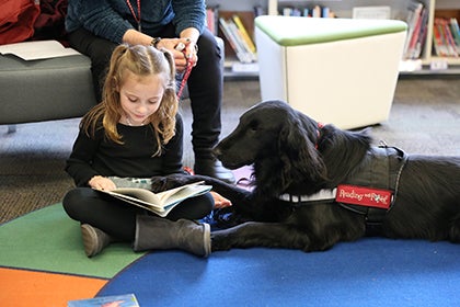 Wedgwood student in black reads to Penny the Reading with Rover dog