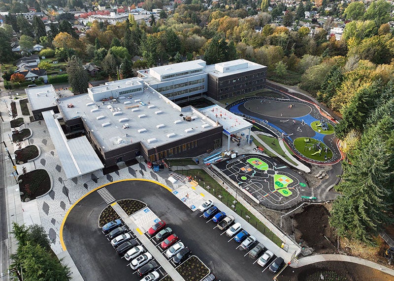 aerial view of a large L-shaped building with planters in front and a parking area with cars in it