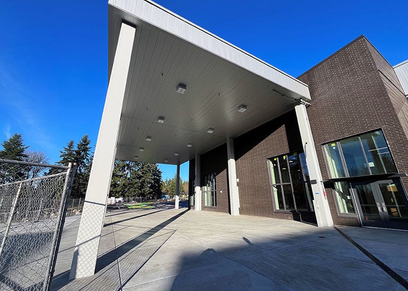 a concrete paved area next to a building has a roof on posts over it