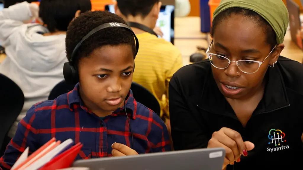 Elementary school student sits with volunteer during week of code to complete coding activity