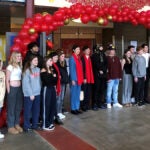 A group of students stand below a red balloon arch in a school hallway