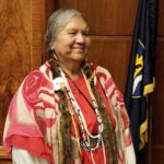 Patsy Whitefoot stands in state capital chambers beside a flag