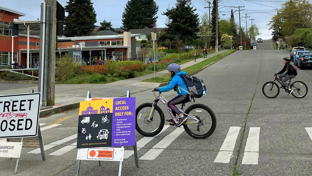 student biking on a school street closed to vehicle traffic with closure sign in foreground.