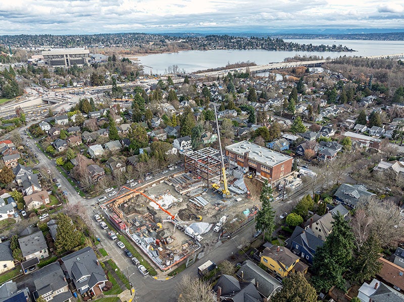 aerial view of a construction site surrounded by streets and houses with a lake and a stadium in the distance