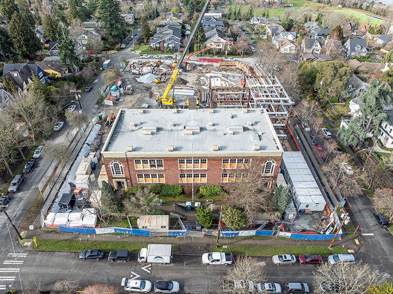 aerial showing a rectangular brick building with construction happening behind it including a crane