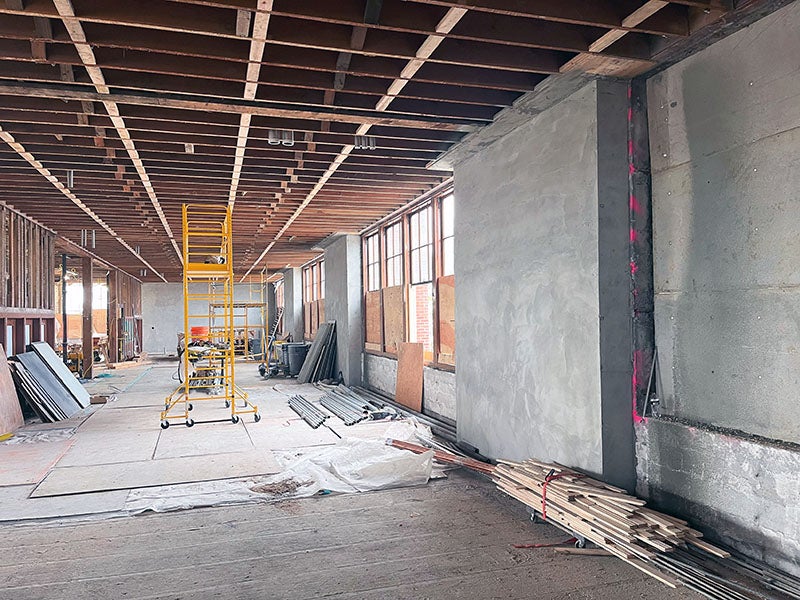 a long room with rafters showing and a concrete wall next to some windows