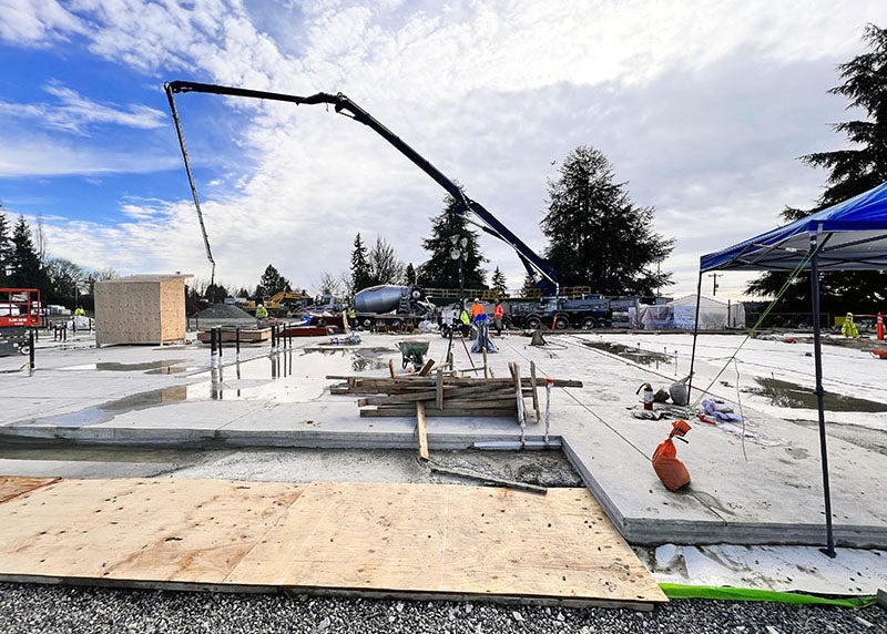 a concrete pump truck in the background with workers and a concrete slab in the foreground