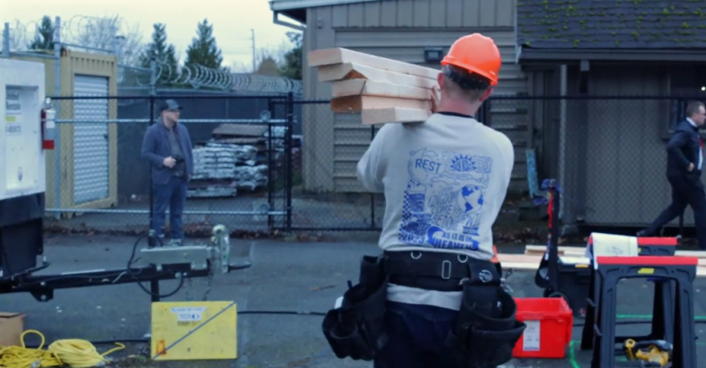 Video still from video produced by SPS students. Still shows student carrying wood and walking through construction site. 
