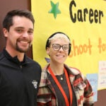 B.F. Day Counselors smile at camera while standing in front of yellow Career Week poster.