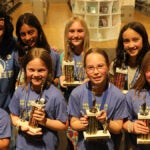 Seven students stand holding their Global Reading Challenge trophies with their teacher.
