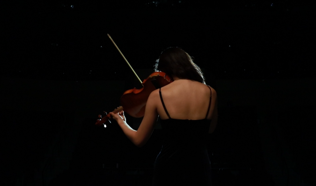 Film still from student film "I Am Blue" featuring a violinist playing from behind and a dark background