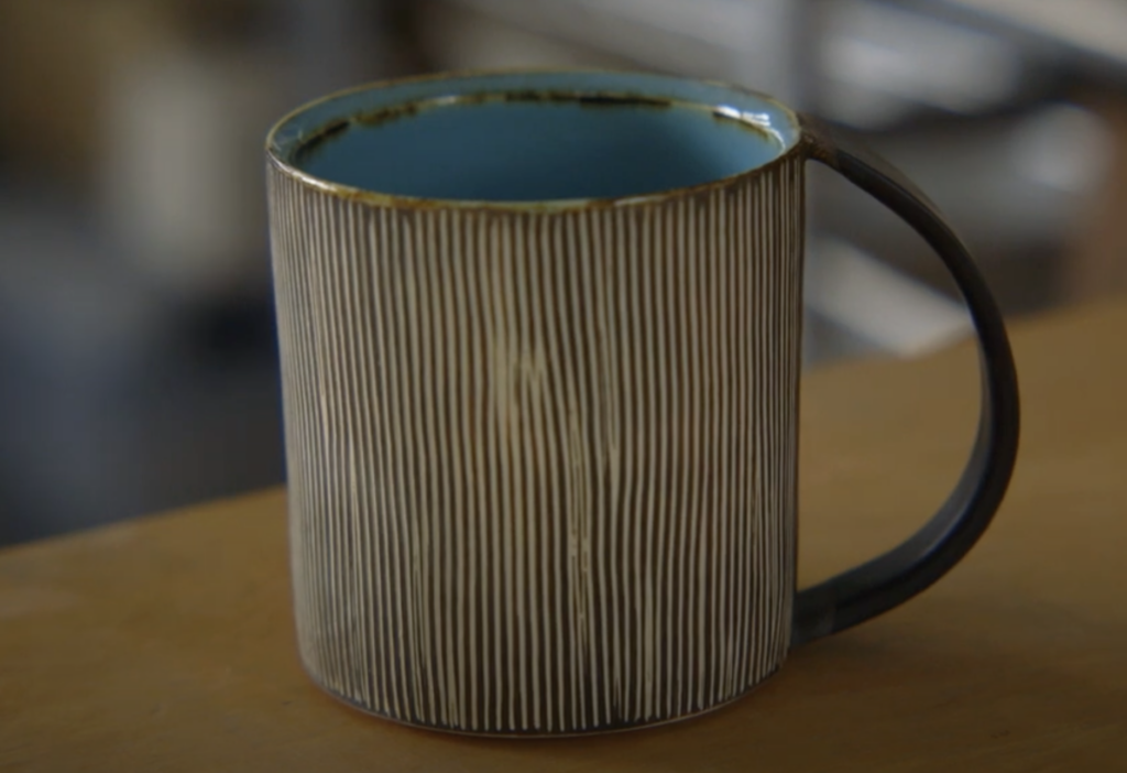 Still from student film "Balancing" with a rustic cup with vertical stripes sitting on a table