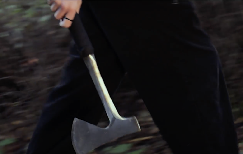 Still from student film "Leave no Trace" with a  person holding an axe and walking