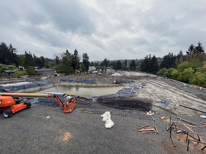 a large muddy area with a retaining pond sits behind a gravel area with a construction machine