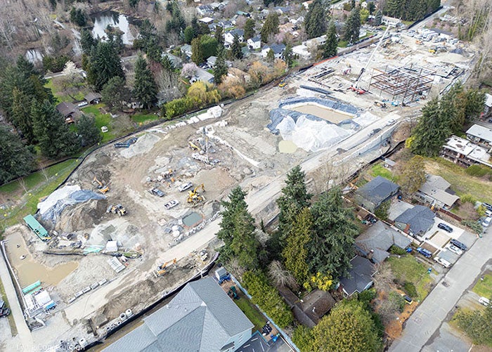 aerial view from the side showing a large construction site iwth steel being erected at one end and trucks and equipment at the other end