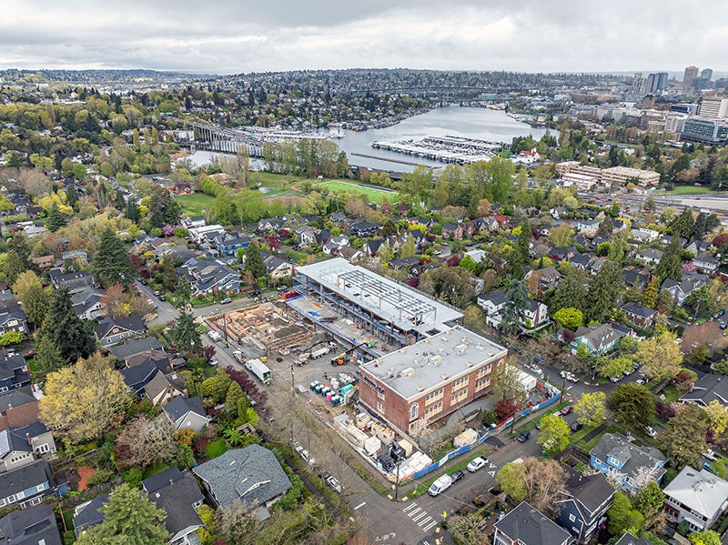 aerial of a brick building with an addition under construction. you can see a body of water in the background