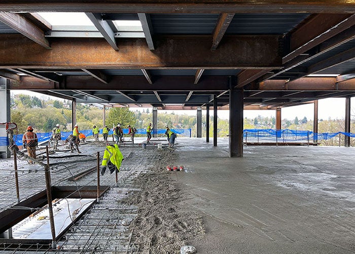 wet concrete covers the floor of a building with steel framing. workers in safety equipment are smoothing the concrete