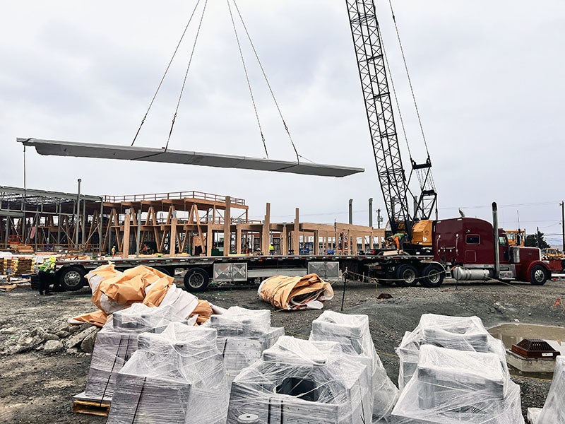 a crane is lowering a large sheet of wood onto a wood frame of a building under construction